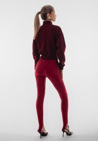 Bordowy sweatshirt z wysokim kołnierzem w komplecie z bordowymi legginsami. Czarne sandały na wysokim obcasie. Gładka faktura, dopasowany krój.