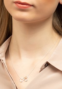 Collana tono argento con due silhouette intrecciate, una delle quali con un accento in oro rosa, appoggiata su uno sfondo tono pelle.