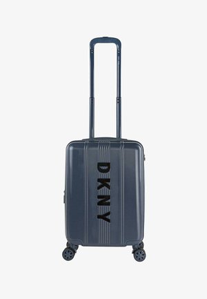 Maleta rígida de color azul oscuro con cuatro ruedas, asa telescópica y logo vertical de DKNY en el frente.