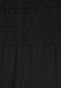 Nahaufnahme von schwarzem Stoff, der oben eine geraffte Textur zeigt, während darunter ein glattes Material fließt, das die weiche Drapierung und Elastizität hervorhebt.