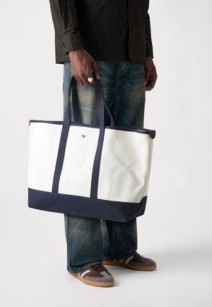 Witte en marineblauwe tote bag met twee duurzame handvatten, gemaakt van textuurmateriaal, met een klein logo op de voorkant en een ruime binnenzijde.