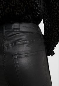 Zwarte denim jeans met een glanzende afwerking, voorzien van een subtiele gestructureerde stof, achterzakken en een merkleren patch aan de tailleband.