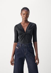 Svart langermet bodysuit med dyp V-hals og samlet midtparti. Kombinert med høyt liv mørk denim brede ben jeans med kontrasterende sømmer.
