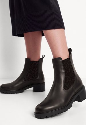 Bottines en cuir noir avec talons épais et empiècements élastiques imprimé léopard portées avec une jupe noire côtelée.