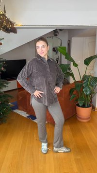 Chemise boutonnée en velours côtelé gris, pantalon côtelé gris et chaussures de sport argentées. Cadre intérieur avec des plantes et un canapé en arrière-plan.