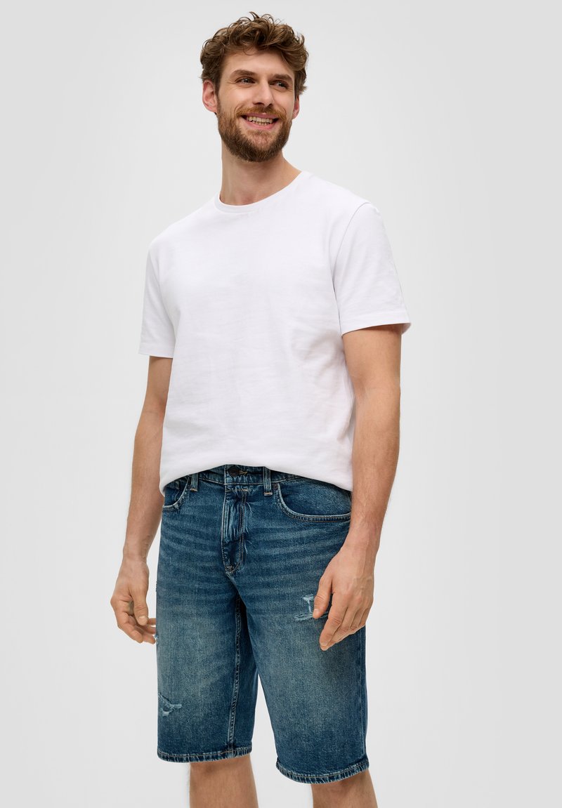 Biała bawełniana koszulka z okrągłym dekoltem, sparowana z niebieskimi szortami dżinsowymi z przetarciami oraz luźnym krojem, sięgającymi do kolan.