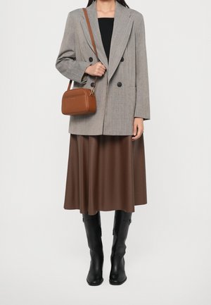 Kobieta w szarej dwurzędowej marynarce, czarnym topie, brązowej spódnicy midi, czarnych kozakach za kolano i z brązową torbą na ramię.