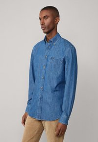 Denim overhemd in blauw, met een enkele borstzak, gouden knoopdetails en lange mouwen. Katoenen corduroy broek in een lichte kleur.