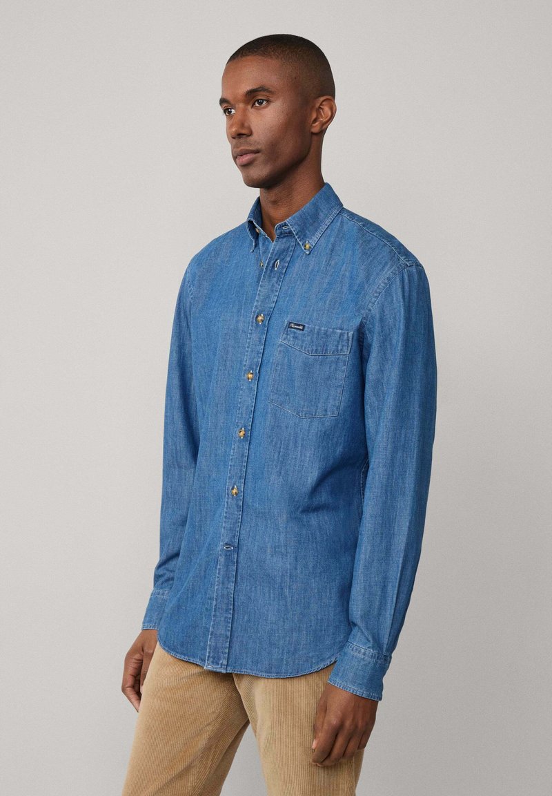 Denim overhemd in blauw, met een enkele borstzak, gouden knoopdetails en lange mouwen. Katoenen corduroy broek in een lichte kleur.