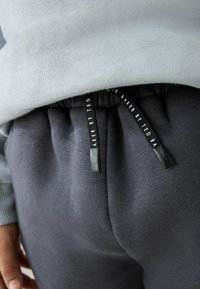Grå sweater møder mørkegrå sweatpants med elastisk talje og snørebånd, der har en tekstureret overflade og glatte accenter.