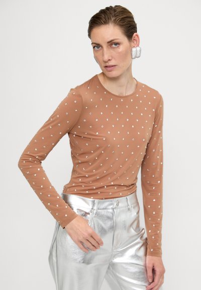 Top cu mâneci lungi de culoare marron, decorat cu aplicații argintii, făcut dintr-un material moale, cu decolteu rotund, asortat cu pantaloni argintii strălucitori. Textură netedă.