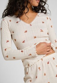 Crèmewit gebreid loungewear set met teddybeerpatronen, voorzien van gerimpelde zooms en een V-hals ontwerp met subtiele textuurdetails.