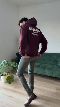 Bordowa bluza z kapturem z napisem "CHAOS STUDIOS" w białym kolorze na plecach, zestawiona z jasnoszarymi, obcisłymi spodniami oraz brązowymi butami na platformie.