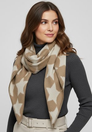 Woman wearing a beige and white star-patterned scarf over a dark gray ribbed sweater and light beige belted pants, looking to the side.