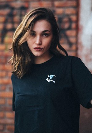 Zwarte katoenen t-shirt met korte mouwen. Bevat een kleine grafische afbeelding van een speler en het nummer "10" in het blauw aan de voorkant.