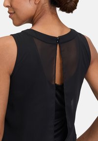 Čierny bezrukávový top s detailom na chrbte vo forme kľúčovej dierky. Obsahuje priesvitnú zadnú panel, hladkú textúru a dva dekoratívne gombíky na krku.