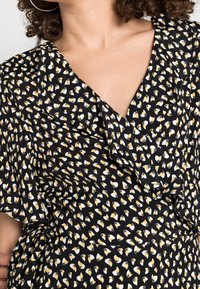 Robe noire avec un motif floral en blanc et jaune, dotée de détails volants et d'un design enroulé, fabriquée à partir d'un tissu léger.