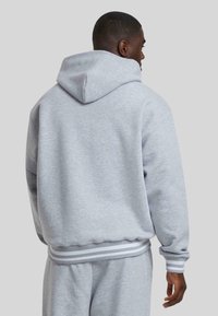 Gray hoodie featuring a hood, ribbed cuffs, and hem. Soft fabric texture with a relaxed fit and small white stripes on the cuffs.