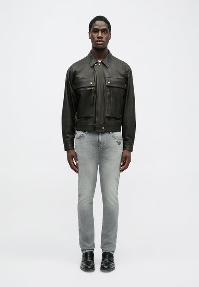 Μαύρο δερμάτινο μπουφάν με δύο μπροστινές τσέπες, χρυσές λεπτομέρειες και κοντή σχεδίαση. Συνδυάζεται με ανοιχτό γκρι τζιν και μαύρα παπούτσια.