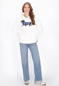 Sudadera con capucha blanca con un gráfico de un dachshund vestido con un suéter azul, que incluye un bolsillo canguro y cordones ajustables.