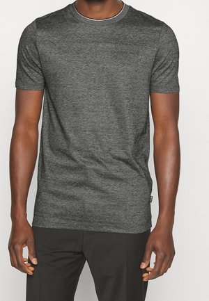 T-shirt a maniche corte grigio scuro con collo rotondo, realizzato in un tessuto testurizzato, con un leggero motivo melangiato. Indossato con pantaloni neri.