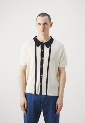 Short-sleeve ribbed shirt in cream with a navy collar, vertical stripes, and buttoned front. Soft texture, relaxed fit, and casual design.