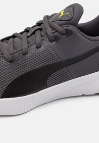 Šedá sportovní bota s texturovaným síťovaným svrškem, hladkými černými akcenty a bílou gumovou podrážkou. Má tkaničky a logo nášivku na jazyku.
