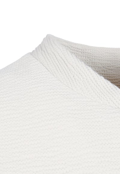 Close-up van een wit gestructureerd gebreide trui met een geribde hoge kraag en zachte stofdetails.