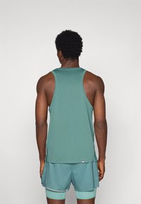 Tank top in teal fabric with a smooth texture, featuring wide armholes and a curved hem. Paired with matching teal shorts.