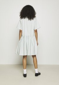 Robe rayée en vert clair et blanc, à manches courtes, jupe froncée avec une forme évasée, associée à des chaussures noires et des chaussettes blanches.