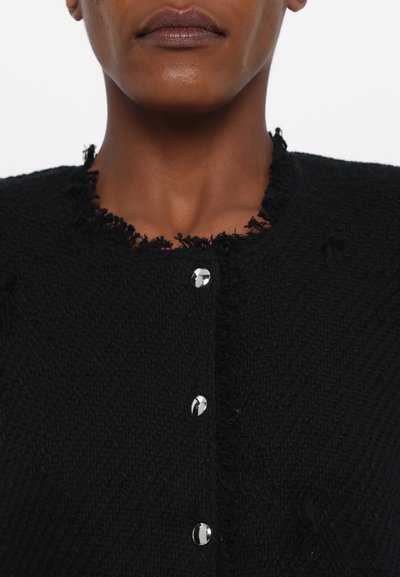 Schwarze Strickjacke mit strukturiertem Muster, ausgefranstem Ausschnitt und sechs metallischen Knopfverschlüssen vorne.