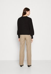 Zwarte pullover trui met opgeblazen mouwen, geribbelde manchetten en zoom, gecombineerd met beige wijde broek en zwarte hoge hakken.