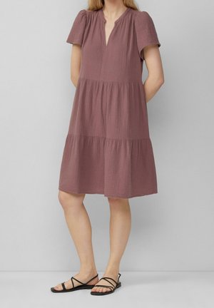 Sukienka z krótkim rękawem w kolorze wrzosowym, z dekoltem w kształcie litery V, marszczonym materiałem i warstwową konstrukcją. Do kompletu czarne sandały na paseczkach. Gładki, teksturowany materiał.