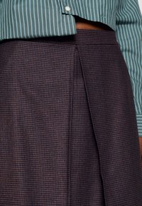 Una gonna a quadri scuri con un design plissettato e una texture liscia, abbinata a una camicia a righe verdi con un davanti bottato.