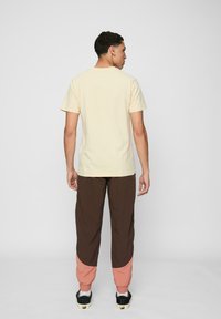 Light yellow cotton t-shirt with a crew neck, paired with brown and pink color-blocked pants. Black shoes with white soles.