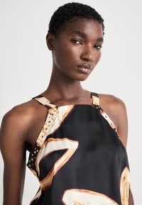 Robe en satin noir avec des motifs abstraits crème et orange, dotée de quincaillerie décorative sur les bretelles et d'une silhouette ajustée.