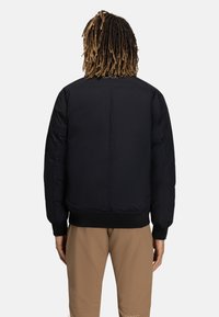 Sort bomberjakke med tekstureret finish, ribbede manchetter og kant. Enkel design uden synlige logoer, set fra ryggen.