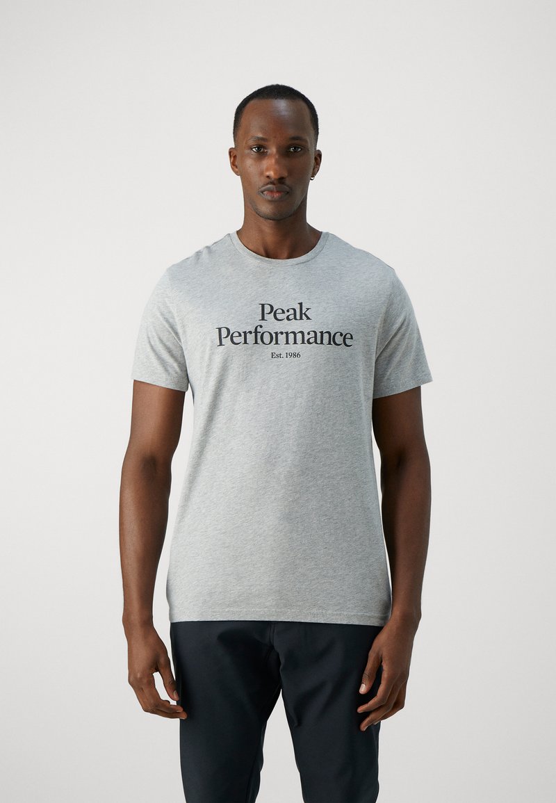 Grå t-skjorte laget av bomull, med korte ermer og rund hals. Fronten har svart tekst "Peak Performance Est. 1986" i en fet skrifttype.