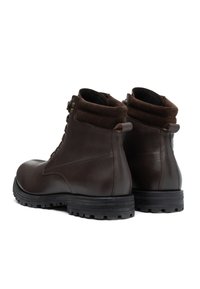 Een paar donkerbruine leren enkelboots met een gevoerde kraag, vetersluiting aan de voorkant en robuuste zwarte rubberen zolen, weergegeven vanuit achter- en zijaanzicht.