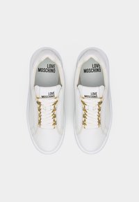 Baskets basses blanches avec œillets dorés, lacets blancs et "LOVE MOSCHINO" imprimé sur la languette et la semelle intérieure, vues de dessus.