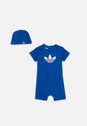 Peto azul para bebé y gorro a juego, ambos con el logotipo blanco de Adidas trefoil, mostrados sobre un fondo blanco.