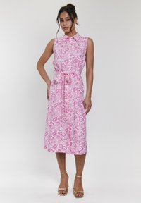 Abito senza maniche di colore rosa con motivi floreali, colletto, cintura in vita e orlo a metà lunghezza. I dettagli includono una silhouette fluida.