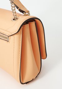 Peach-colored handbag with textured material, contrasting dark trim, zipper detail, and a chain strap. Expands at the sides for shape.