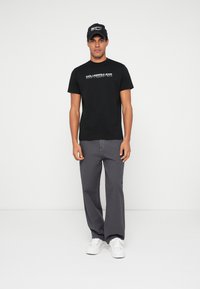 Melnas kokvilnas T-krekls ar logo priekšpusē, apvienots ar pelēkiem plašiem biksēm un baltām sporta kurpēm. Aksesuāri ietver melnu cepuri ar logo.