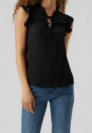 Blusa nera con maniche arricciate e chiusura al collo con fiocco. Tessuto morbido, vestibilità ampia, design minimalista. Indossata con jeans blu.