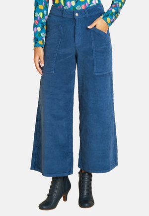 Wide-legged blue corduroy pants with two front pockets. Textured fabric and a button closure at the waist. Paired with black lace-up ankle boots.