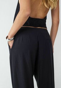 Czarne spodnie w poziome paski o luźnym kroju, z bocznymi kieszeniami i gładką teksturą, zestawione z bluzką bez pleców z marszczonym detalem.