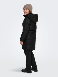 Black puffer jacket with a textured design, hood, and button details, paired with black pants and a light brown knit beanie.