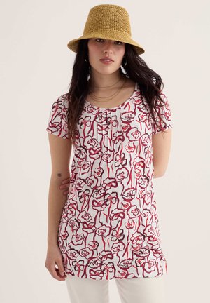 Naine, kes kannab valget tunikat punase lillemustriga, sinepikollast kootud mütsi, kuldseid rõngaskõrvarõngaid ja kihilisi kuldseid kaelakeesid.