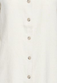 Nahaufnahme eines elfenbeinfarbenen Leinenstoffs mit fünf beigen Plastikknöpfen, die vertikal in der Mitte ausgerichtet sind.